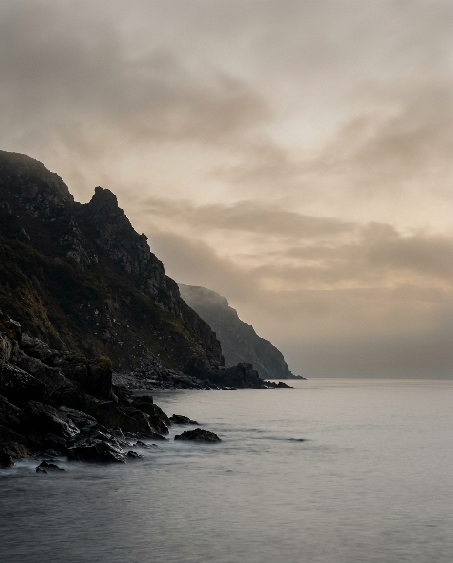 A calm grey sea below dark headland cliffs under a hazy sky